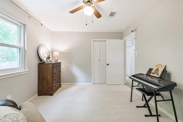 interior space featuring baseboards, visible vents, a ceiling fan, and light colored carpet