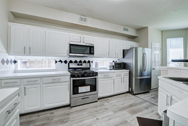 kitchen featuring appliances with stainless steel finishes, backsplash, white cabinetry, light countertops, and light wood finished floors