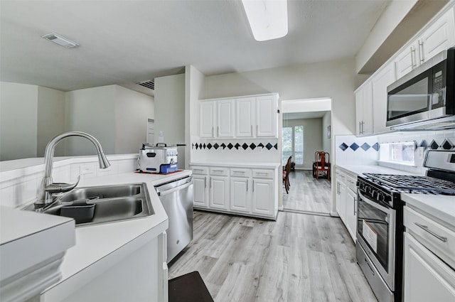 kitchen featuring appliances with stainless steel finishes, a sink, light wood-style floors, white cabinetry, and light countertops