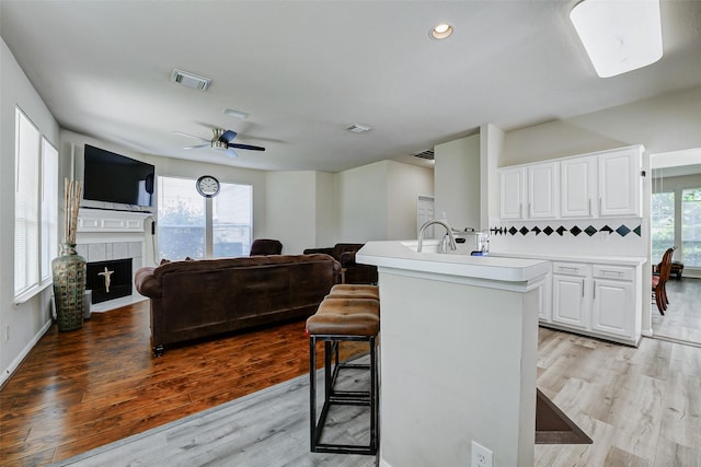kitchen with light countertops, a kitchen island with sink, white cabinetry, a breakfast bar area, and light wood-type flooring