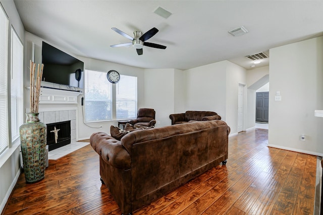 living room featuring wood-type flooring, ceiling fan, a tile fireplace, and baseboards