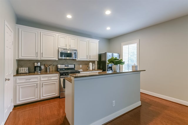 kitchen with white cabinets, stainless steel appliances, decorative backsplash, and dark wood-type flooring