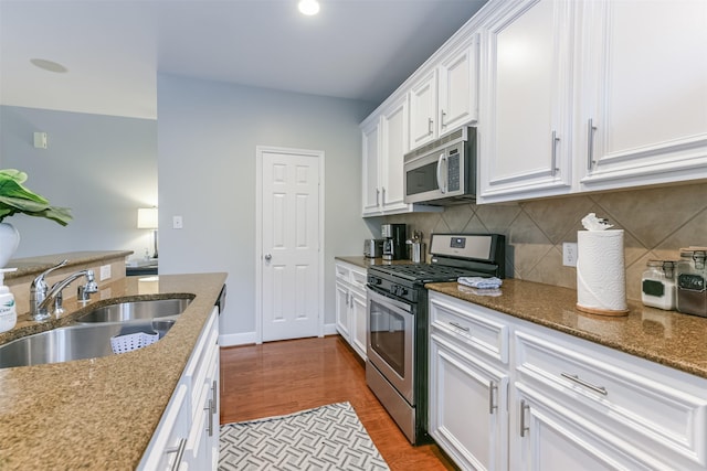 kitchen featuring tasteful backsplash, wood finished floors, a sink, stainless steel appliances, and white cabinetry