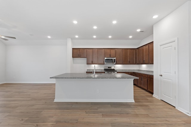 kitchen with stainless steel appliances, a kitchen island with sink, a sink, light wood-style floors, and ceiling fan
