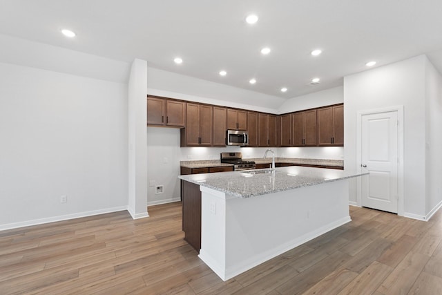 kitchen featuring light stone counters, a sink, light wood-style floors, stainless steel appliances, and a center island with sink
