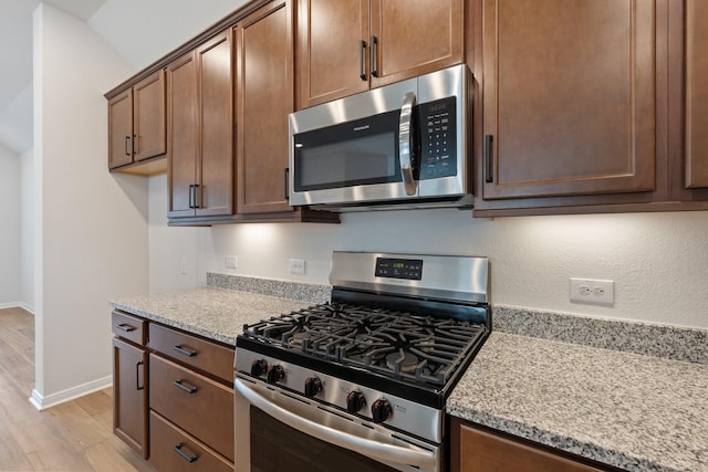 kitchen featuring baseboards, light stone countertops, stainless steel appliances, and light wood-style flooring