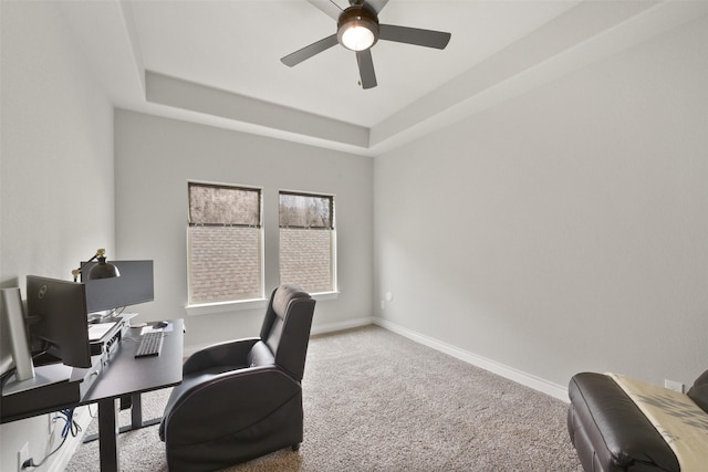 carpeted office with baseboards, a tray ceiling, and ceiling fan