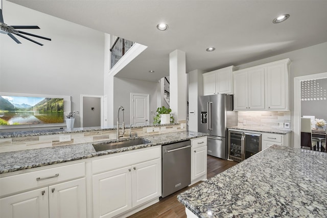 kitchen with beverage cooler, light stone counters, a sink, appliances with stainless steel finishes, and dark wood-style flooring