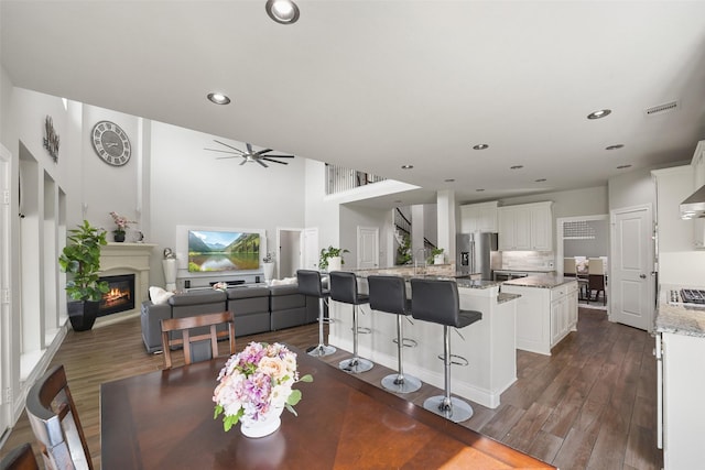 kitchen featuring a glass covered fireplace, visible vents, stainless steel refrigerator with ice dispenser, dark wood-style floors, and a kitchen island