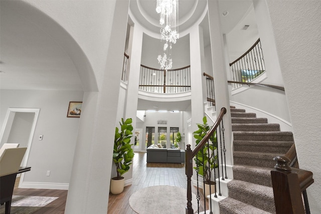 entrance foyer featuring stairway, a towering ceiling, wood finished floors, arched walkways, and a notable chandelier