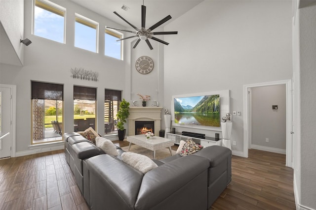 living area featuring ceiling fan, a high ceiling, a warm lit fireplace, and wood finished floors