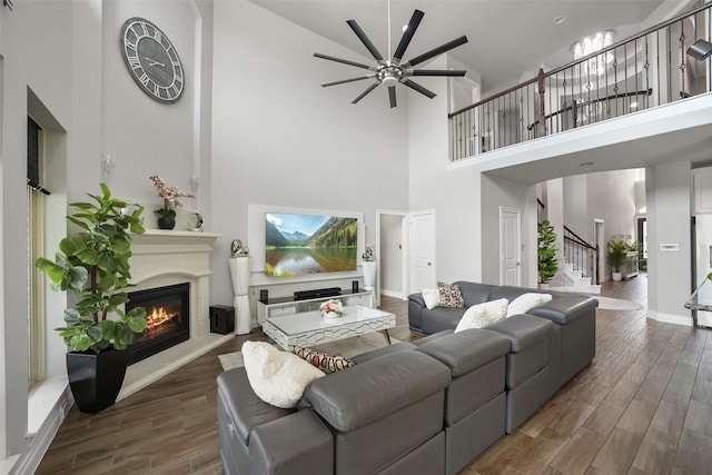 living room with a glass covered fireplace, a ceiling fan, stairs, high vaulted ceiling, and dark wood-type flooring