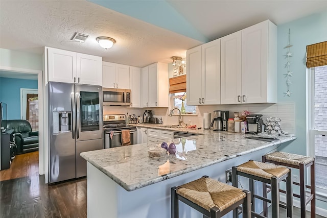 23001 Fresca St, Galveston, TX 77554 - kitchen with stainless steel appliances, a peninsula, dark wood-style floors, light stone countertops, and white cabinetry