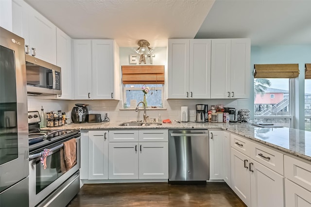 23001 Fresca St, Galveston, TX 77554 - kitchen with appliances with stainless steel finishes, a sink, white cabinets, dark wood-style flooring, and light stone countertops