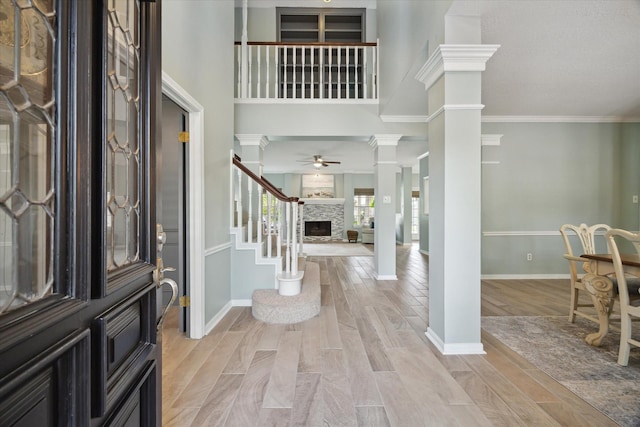 foyer with crown molding, decorative columns, a fireplace, ceiling fan, and stairway