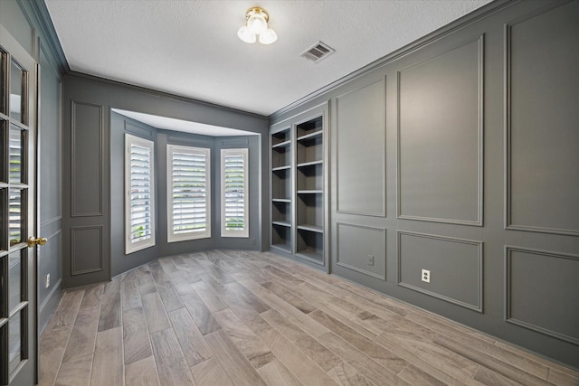 unfurnished room with visible vents, ornamental molding, a textured ceiling, and a decorative wall
