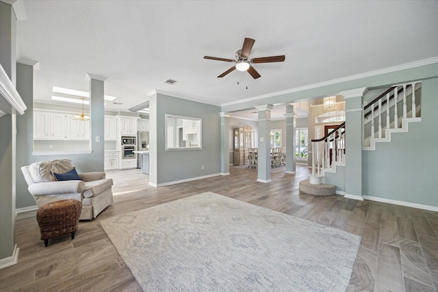 living area with ceiling fan with notable chandelier, decorative columns, visible vents, ornamental molding, and stairway