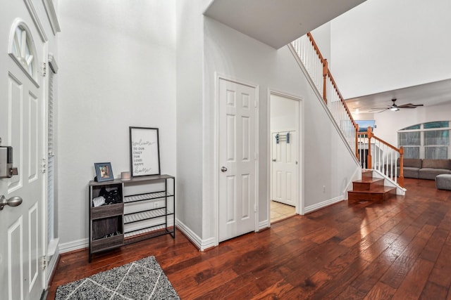entryway featuring wood-type flooring, stairs, a ceiling fan, a towering ceiling, and baseboards