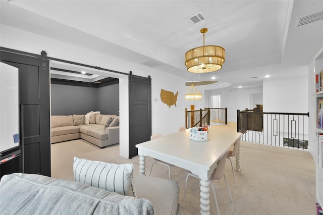 living area featuring a barn door, visible vents, light colored carpet, and a tray ceiling