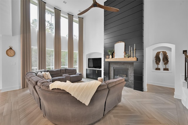 living room featuring a glass covered fireplace, a ceiling fan, a high ceiling, and a healthy amount of sunlight