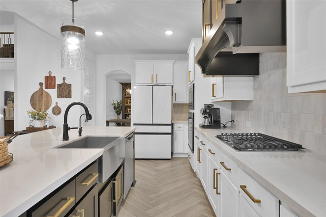kitchen with pendant lighting, stainless steel appliances, light countertops, wall chimney exhaust hood, and white cabinetry