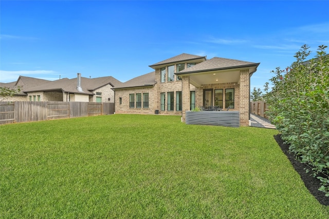 back of property with a fenced backyard, brick siding, a yard, and a shingled roof