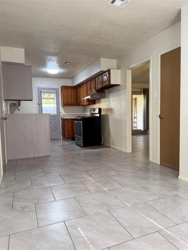 kitchen with a textured ceiling, gas stove, under cabinet range hood, and visible vents