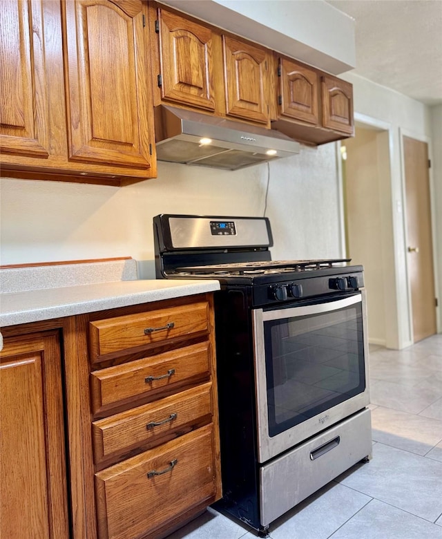 kitchen with brown cabinetry, stainless steel gas range, under cabinet range hood, and light countertops
