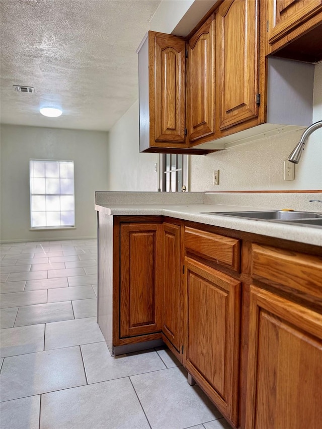 kitchen featuring a sink, a textured ceiling, visible vents, brown cabinetry, and light countertops