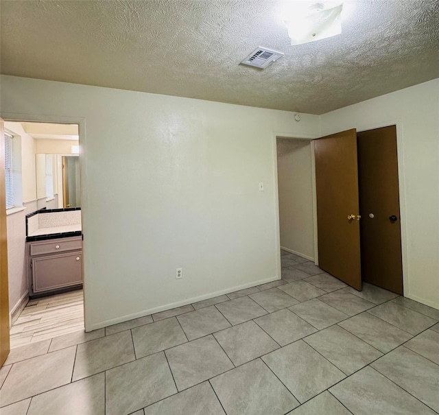 unfurnished bedroom with visible vents, light tile patterned flooring, a closet, baseboards, and a textured ceiling