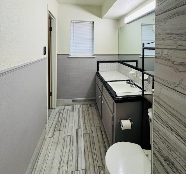 bathroom featuring a wainscoted wall, toilet, tile walls, wood finished floors, and vanity