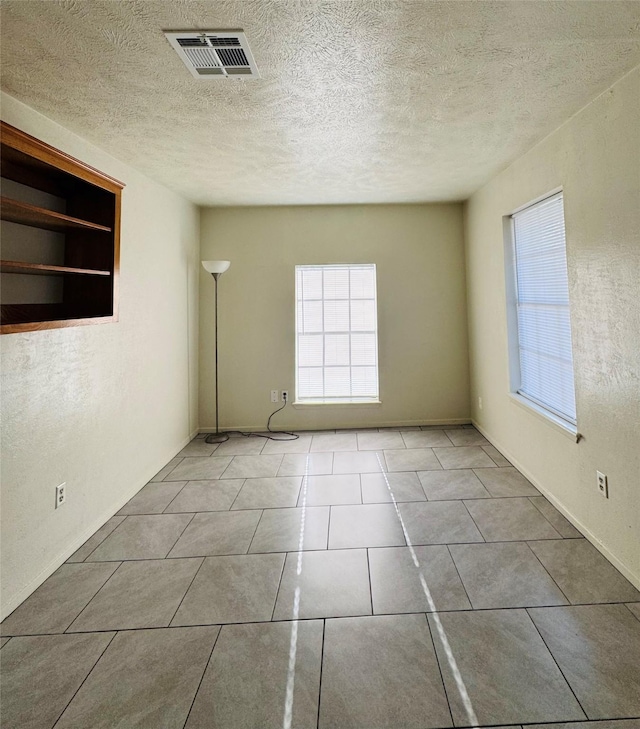 spare room featuring tile patterned flooring, a textured ceiling, and visible vents