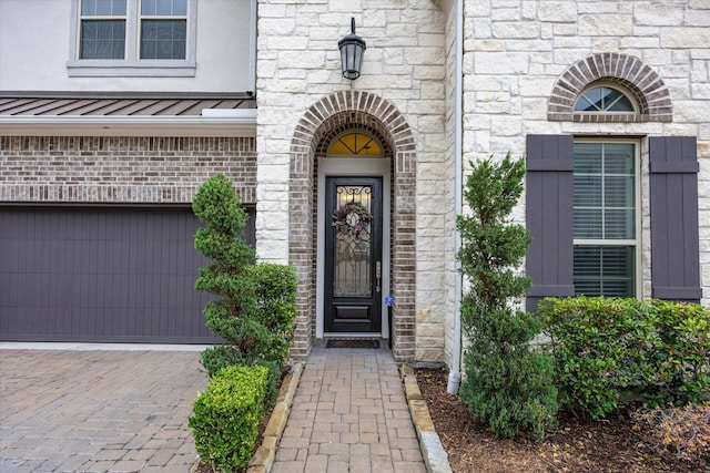 view of exterior entry featuring stone siding, a standing seam roof, brick siding, metal roof, and driveway