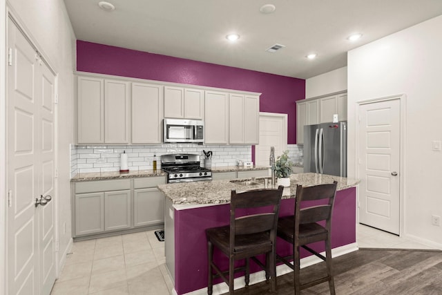 16231 Westley Ridge Dr, Hockley, TX 77447 - kitchen with stainless steel appliances, an island with sink, backsplash, a sink, and light stone countertops