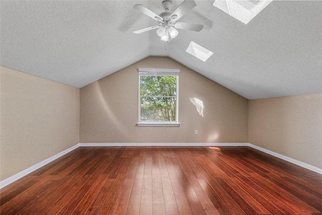 bonus room featuring a textured ceiling, dark wood finished floors, baseboards, vaulted ceiling with skylight, and ceiling fan