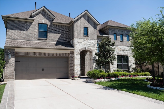 french provincial home featuring a shingled roof, concrete driveway, stone siding, brick siding, and a garage