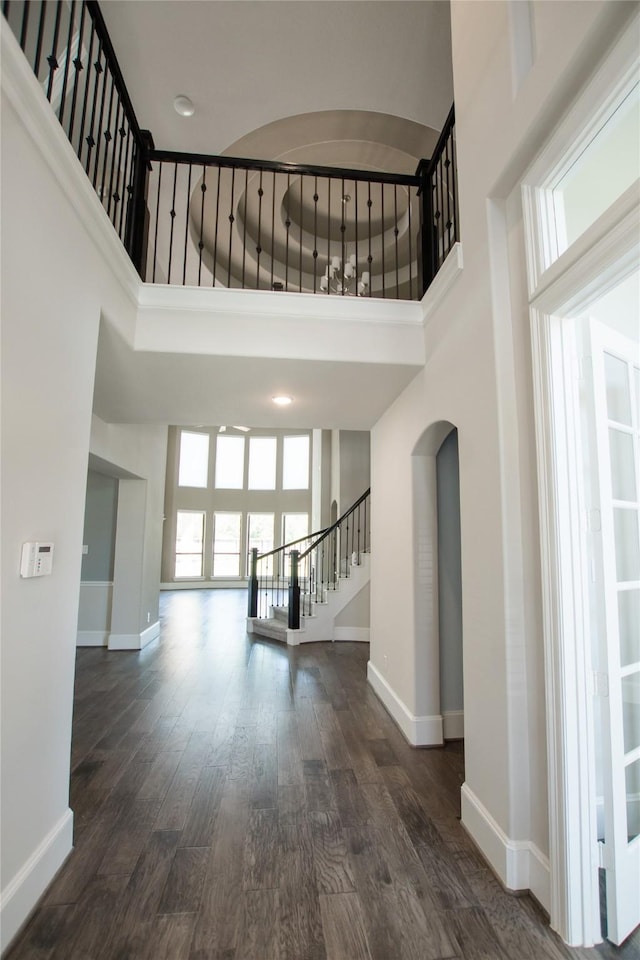 entrance foyer featuring stairs, arched walkways, baseboards, a high ceiling, and dark wood-type flooring