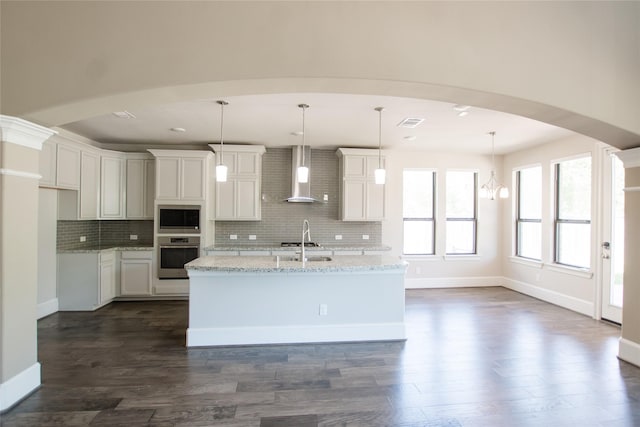 kitchen with backsplash, wall chimney exhaust hood, appliances with stainless steel finishes, and dark wood-style flooring