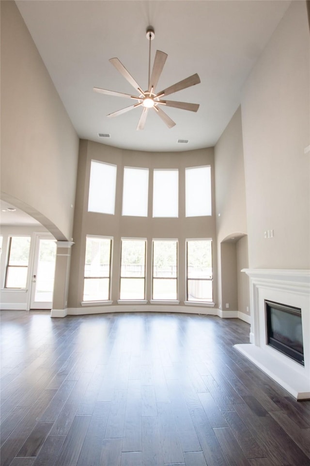 unfurnished living room with a glass covered fireplace, a towering ceiling, arched walkways, and ceiling fan