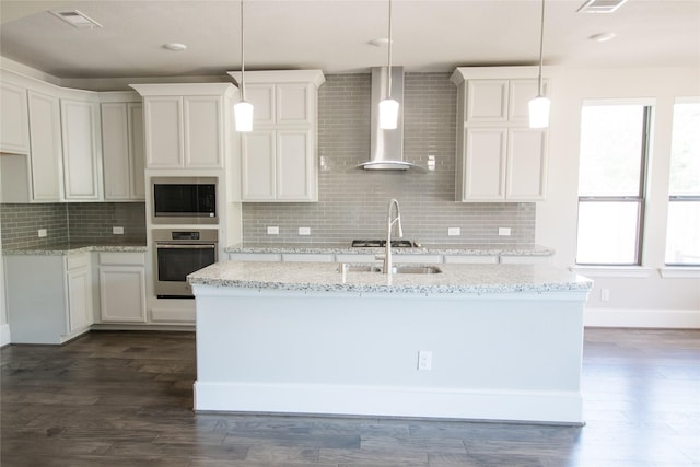 kitchen featuring stainless steel appliances, visible vents, wall chimney exhaust hood, decorative backsplash, and a kitchen island with sink