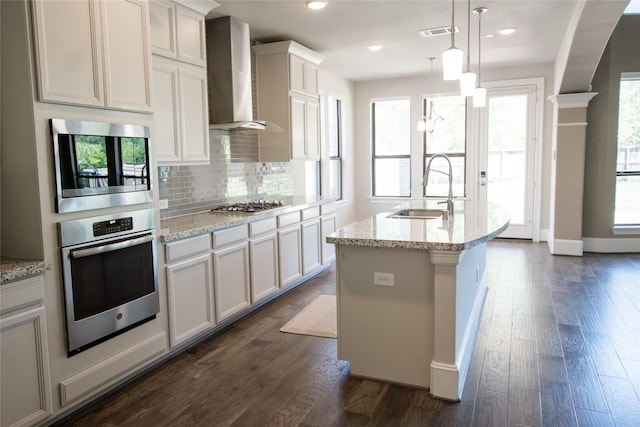 kitchen with stainless steel appliances, a sink, tasteful backsplash, light stone counters, and wall chimney range hood