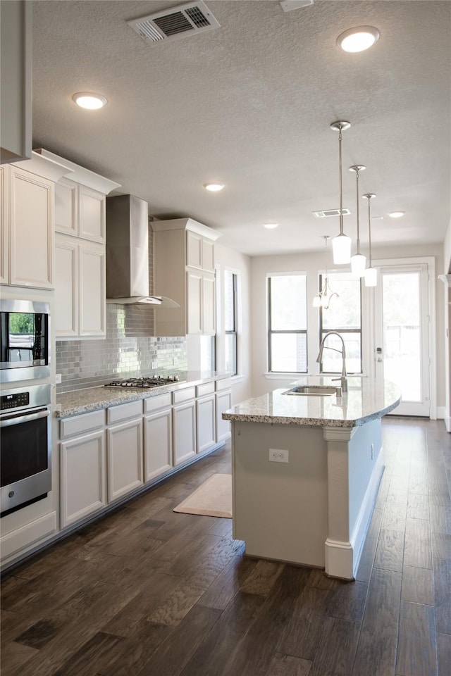 kitchen featuring wall chimney range hood, a sink, visible vents, appliances with stainless steel finishes, and dark wood-style floors