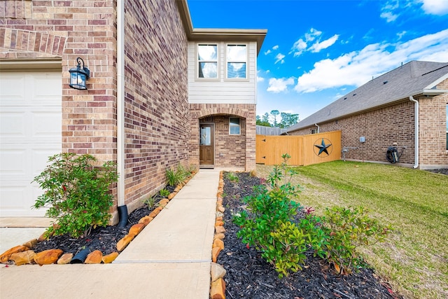 entrance to property featuring brick siding, a yard, an attached garage, and fence