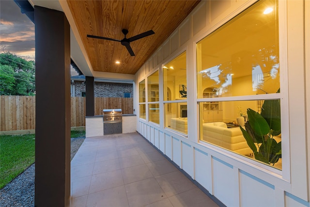 patio terrace at dusk featuring exterior kitchen, a ceiling fan, and fence