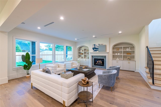 living room featuring stairway, light wood-style flooring, a fireplace, baseboards, and visible vents