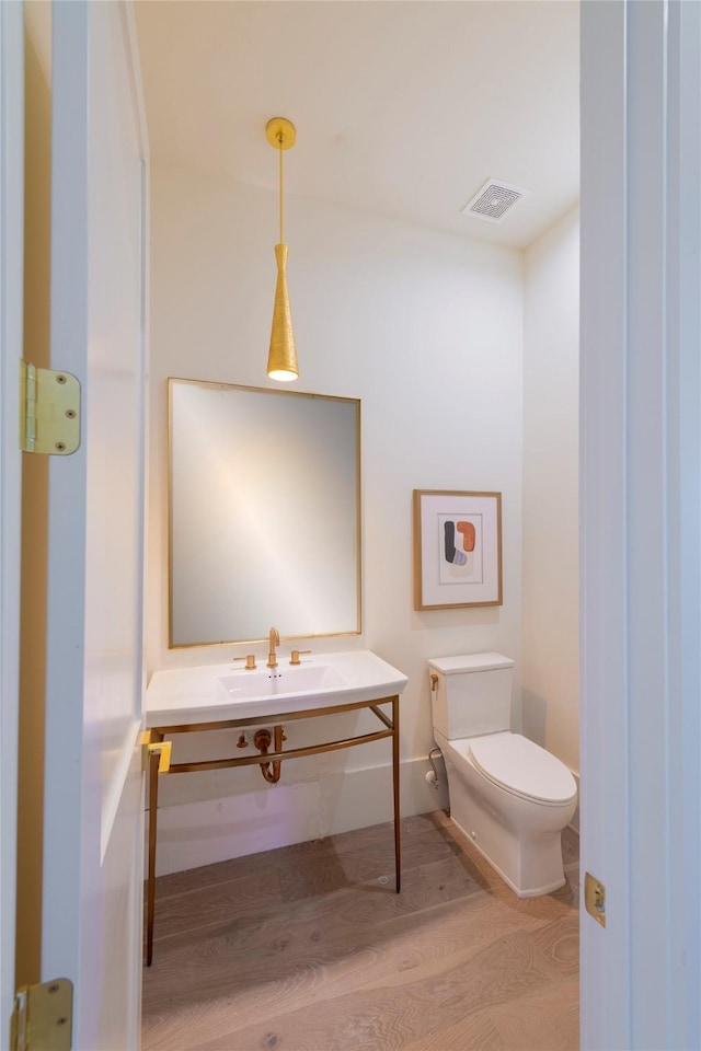 half bathroom featuring wood finished floors, vanity, baseboards, toilet, and visible vents