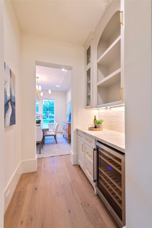 bar with light wood finished floors, wine cooler, backsplash, a dry bar, and baseboards