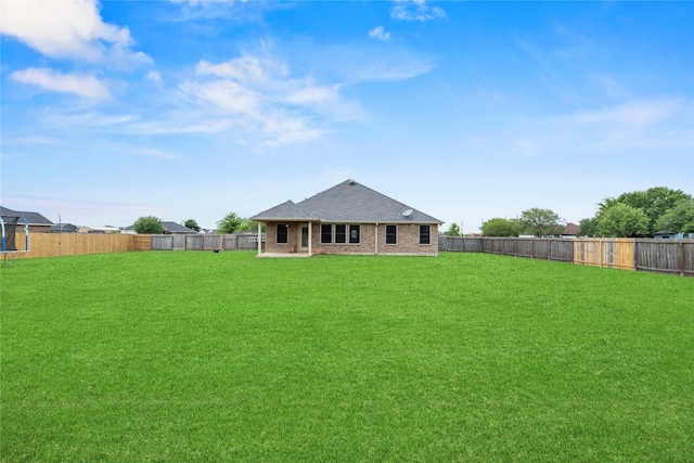 rear view of property featuring a fenced backyard, brick siding, a yard, and roof with shingles