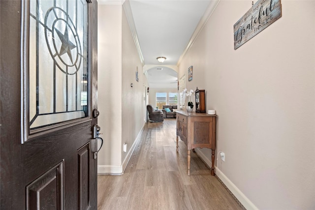 foyer entrance featuring light wood-style flooring, baseboards, arched walkways, and ornamental molding