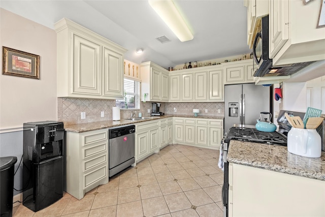 kitchen featuring light stone counters, stainless steel appliances, backsplash, a sink, and cream cabinets